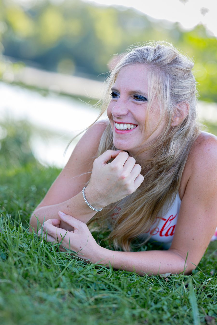 Femme blonde souriante allongée dans l'herbe au bord de l'eau