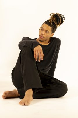 Homme aux dreadlocks assis en tenue noire, photo studio