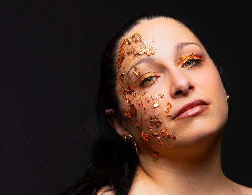 Portrait d'une femme au maquillage pailleté orange sur fond noir