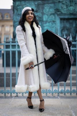 Femme en long manteau blanc avec un parapluie devant les grilles de la place Vendôme