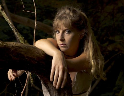 Portrait en forêt d'une femme accoudée à une branche, ambiance sombre