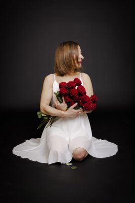 Femme en robe blanche assise au sol avec un bouquet de roses rouges